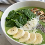 A healthy glowing green smoothie bowl with spinach, kale, avocado, chia seeds, coconut flakes, and banana slices.